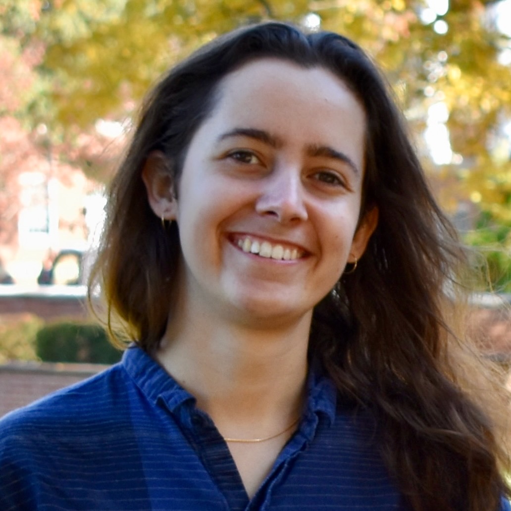 Close portrait of a young woman standing outside with fall leaves in the background.