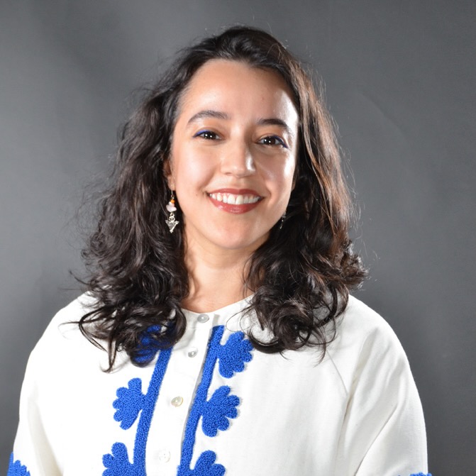 Portrait of a young woman, wearing a white tunic with blue embroidery.