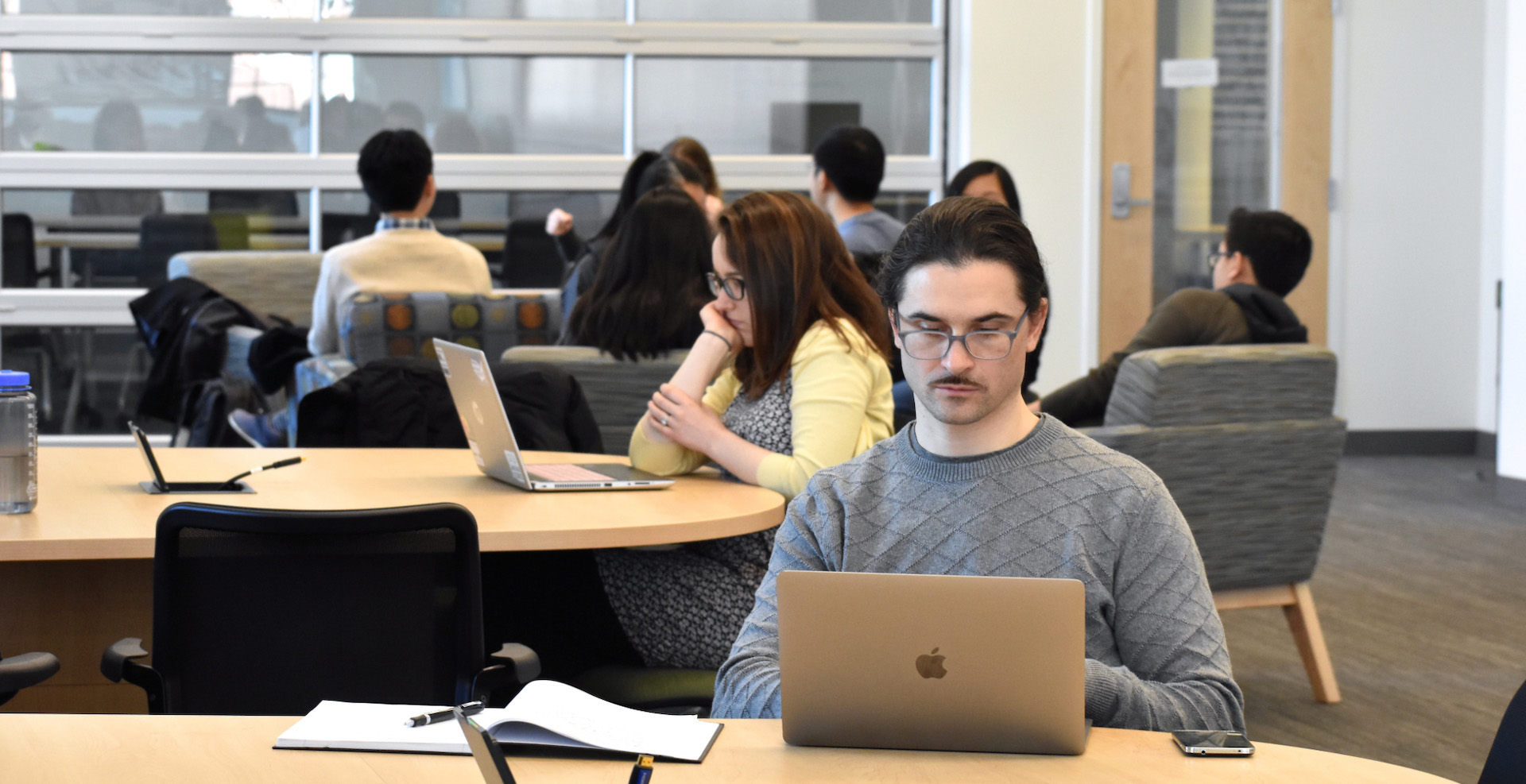 Student is studying on his laptop in the Language Science Center, with other students sitting behind him in the background